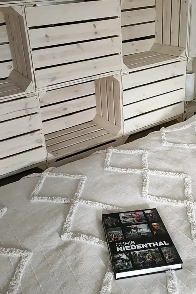 Poddasze Czytanie. Przytulne łóżko z jasną pościelą na Poddaszu Łuby Siedem, na tle drewnianej ażurowej ścianki. Na łóżku widoczna album Chrisa Niedenthala, sprzyjający wypoczynkowi i refleksji.