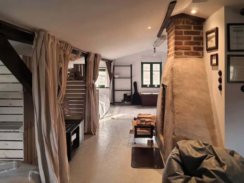 Poddasze. Wnętrze Poddasza Łuby Siedem: boczna ściana glinianej baby, zabytkowa toaletka, drewniane belki i ażurowe ścianki ze skrzynek, oddzielające alkowy lnianymi zasłonami.