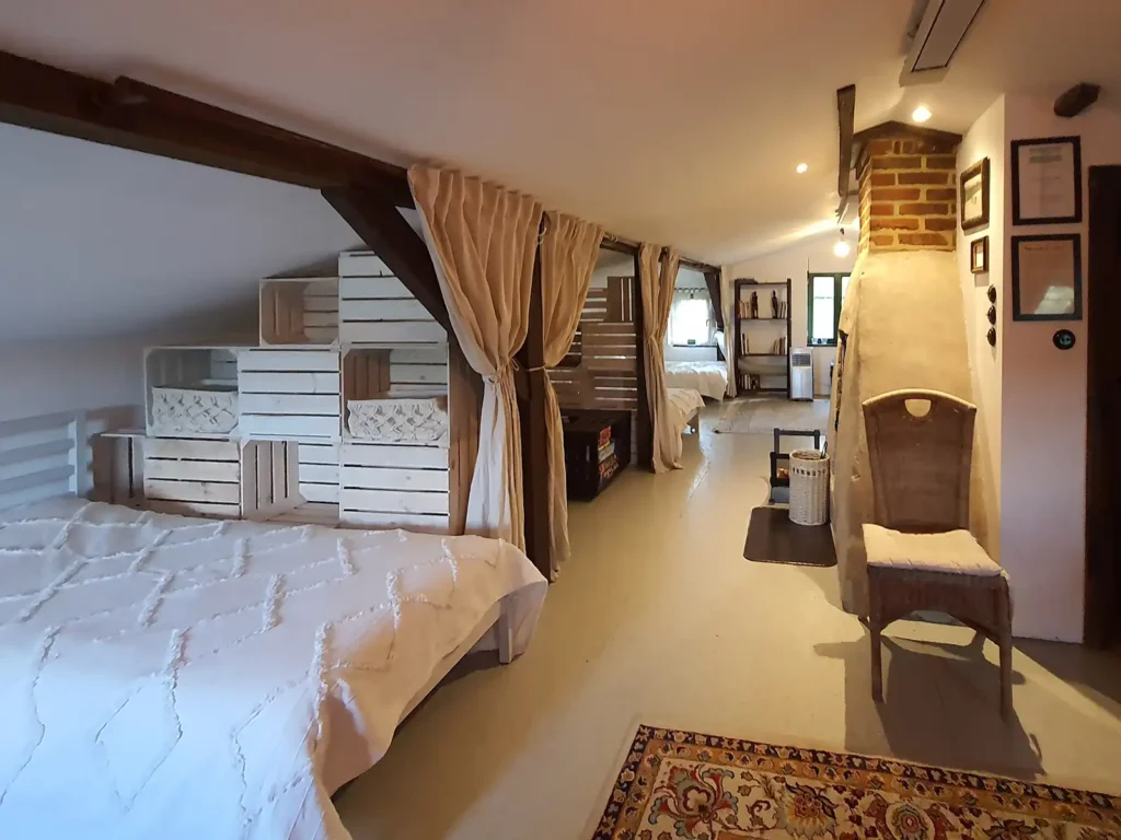 Poddasze. Widok ogólny na jasne poddasze dla 10 osób w Domu Gościnnym Łuby Siedem. Ażurowe ścianki z drewna, kominek i wiklinowe detale podkreślające styl slow life. Idealny nocleg dla grupy w Borach Tucholskich.