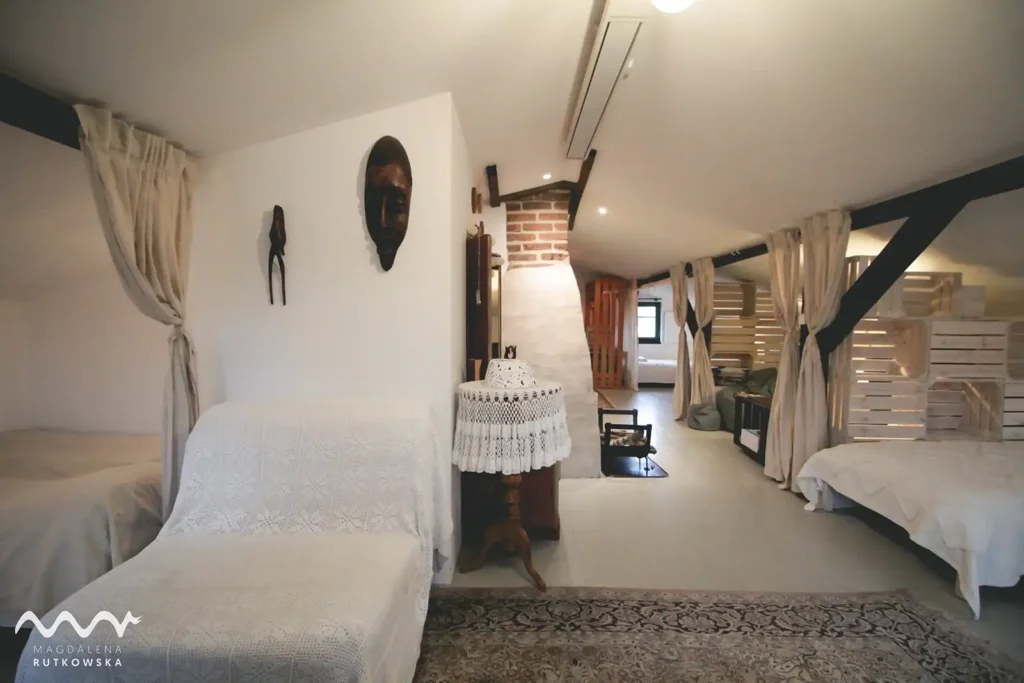 Poddasze. Przytulny fotel z narzutą na Poddaszu Łuby Siedem, obok ścianki z drewnianych skrzynek, maski afrykańskie.