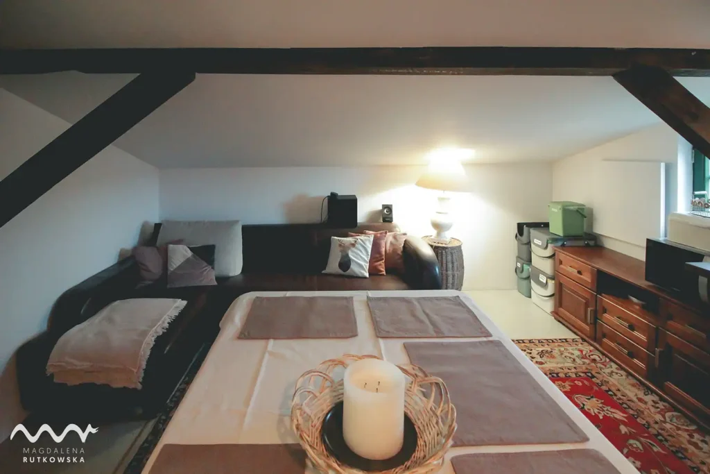 Poddasze, jadalnia. Jadalnia z aneksem kuchennym na Poddaszu Łuby Siedem. Zabytkowy stół rozkładany na korbkę (do 10 osób) i wygodna kanapa. Wnętrze z drewnianymi belkami, idealne do wspólnego biesiadowania w Borach Tucholskich.