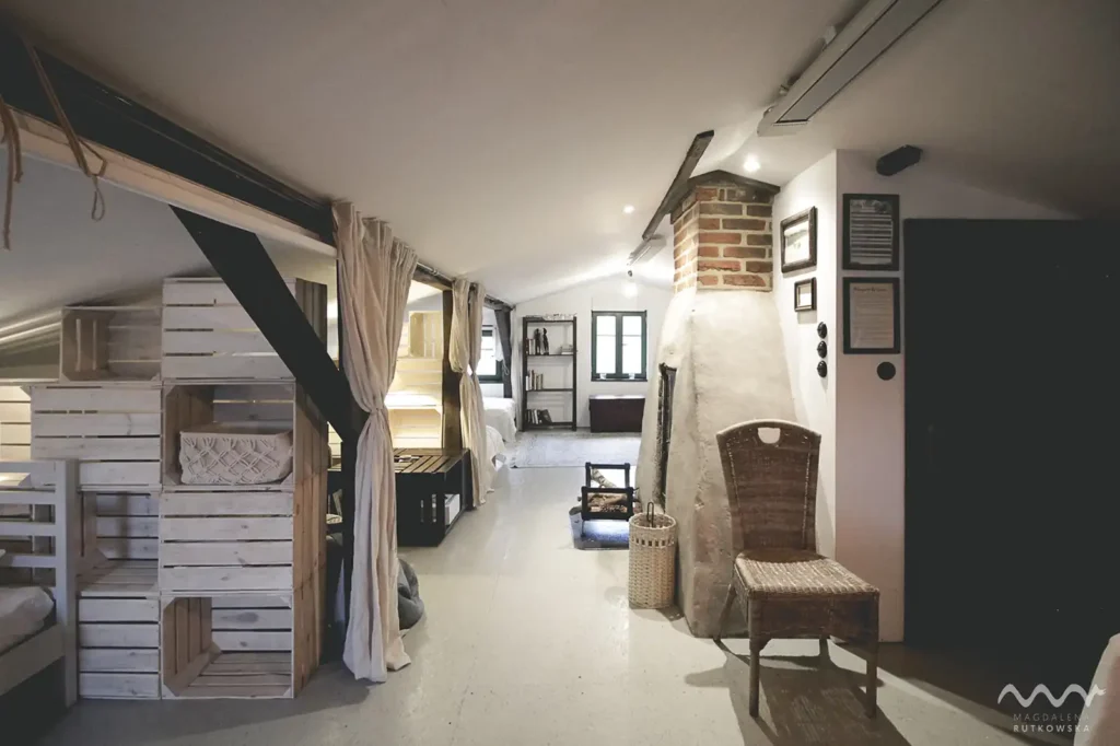 Poddasze. Widok ogólny na jasne poddasze dla 10 osób w Domu Gościnnym Łuby Siedem. Ażurowe ścianki z drewna, kominek i wiklinowe detale podkreślające styl slow life. Idealny nocleg dla grupy w Borach Tucholskich.